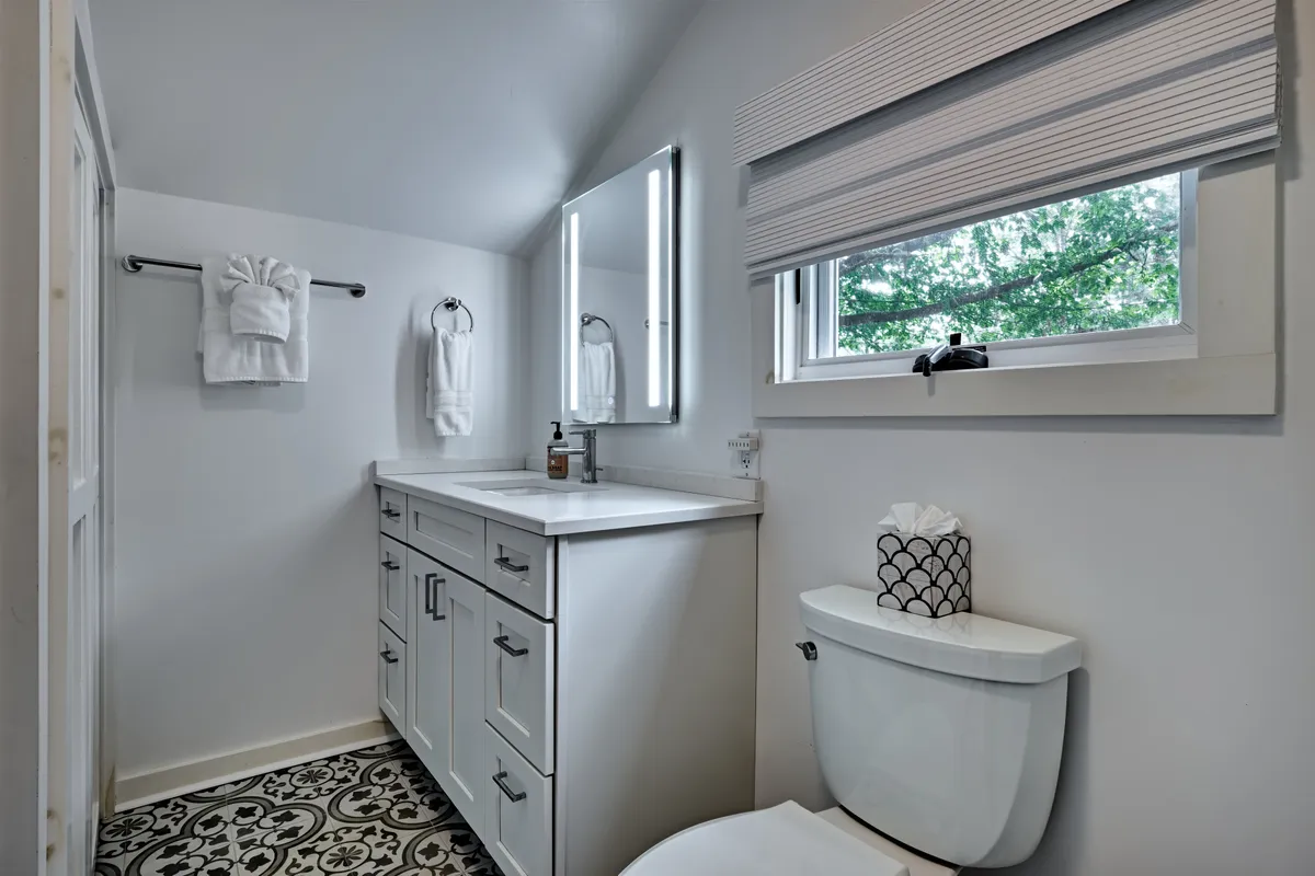 This image features a well-lit vanity with a modern sink, an LED-lit mirror, decorative tile flooring, and a window letting in natural light. The inviting setup suggests a soothing environment for personal grooming and morning routines.