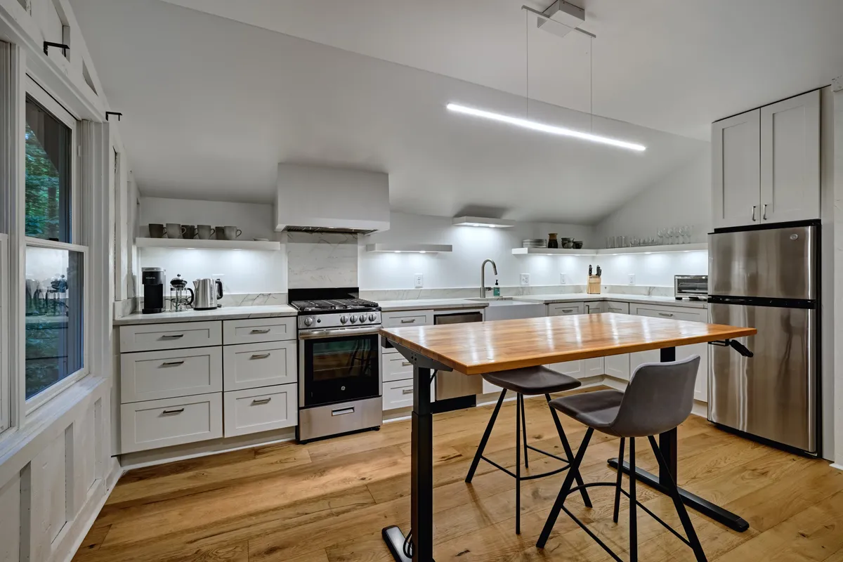 This image captures a modern kitchen with sleek stainless steel appliances, a central island with seating, and crisp white cabinetry. The layout feels open and welcoming, ideal for cooking and casual dining. The kitchen is well-lit, suggesting a bright and functional space for preparing meals or enjoying morning coffee.