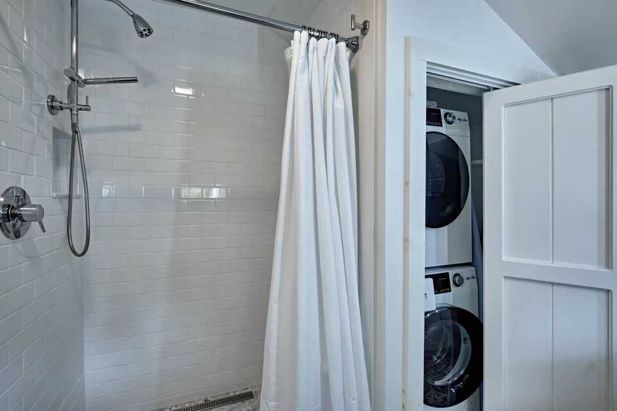 The image displays a modern shower area adjacent to laundry appliances, providing a glimpse into a functional yet calming space. The design emphasizes practicality with rejuvenation, ideal for solo travelers and remote workers seeking comfort.